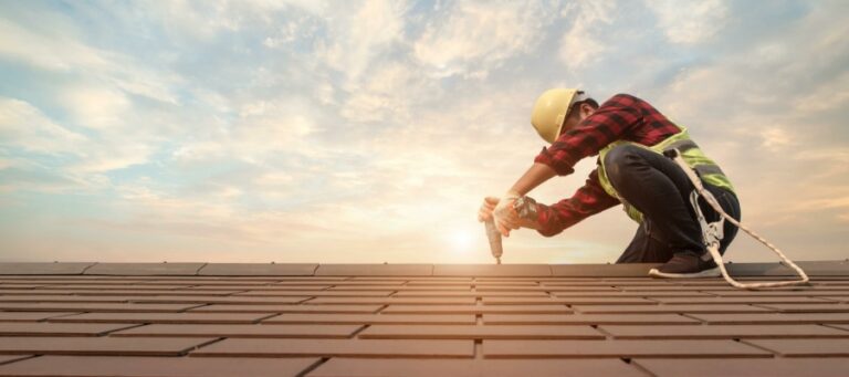 tradesman nails down shingles atop a roof