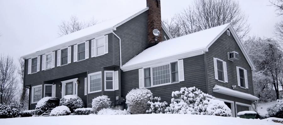 a suburban home with a layer of snow on the roof and yard