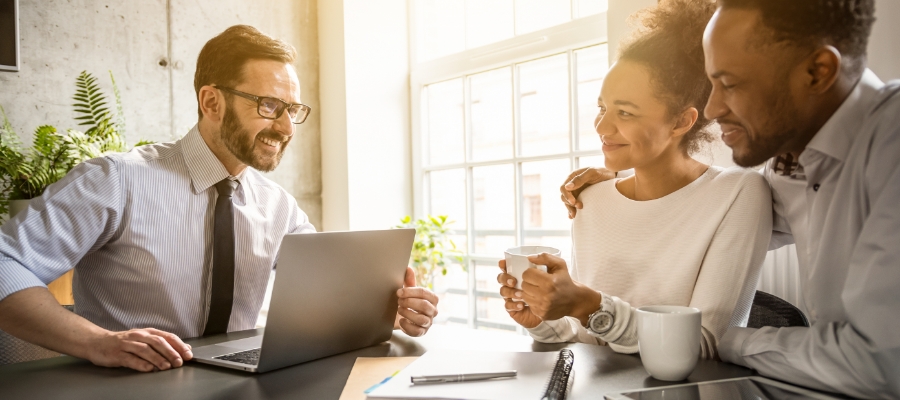 a couple smiles on one side of a table with an insurance worker on the other