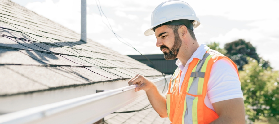 a man in a construction hat and vest inspects a gutter